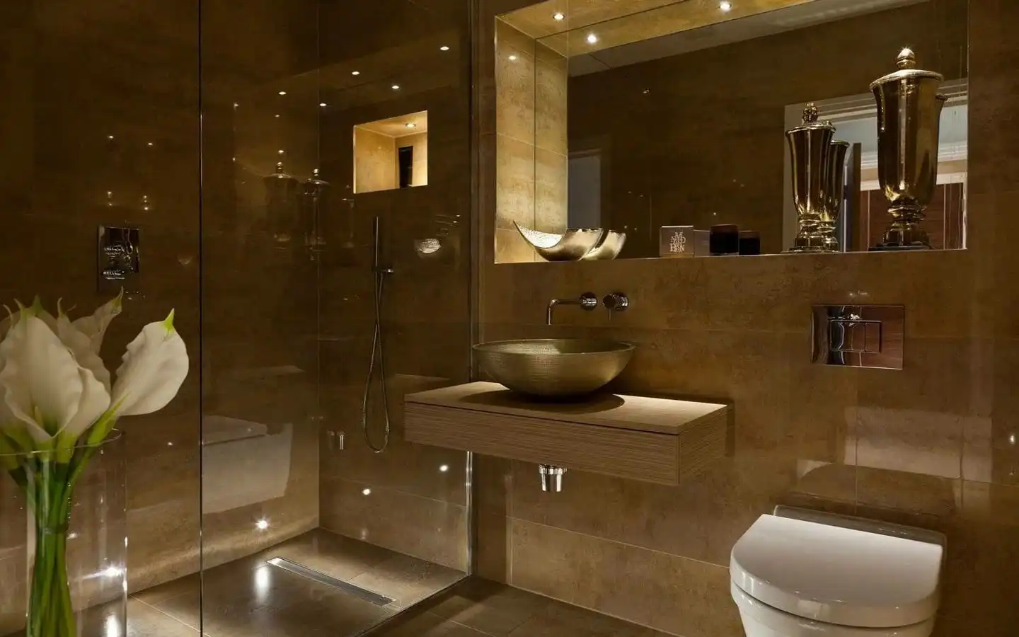 Modern luxury bathroom with brown marble walls, glass shower, wall-mounted vanity sink, and soft ambient lighting