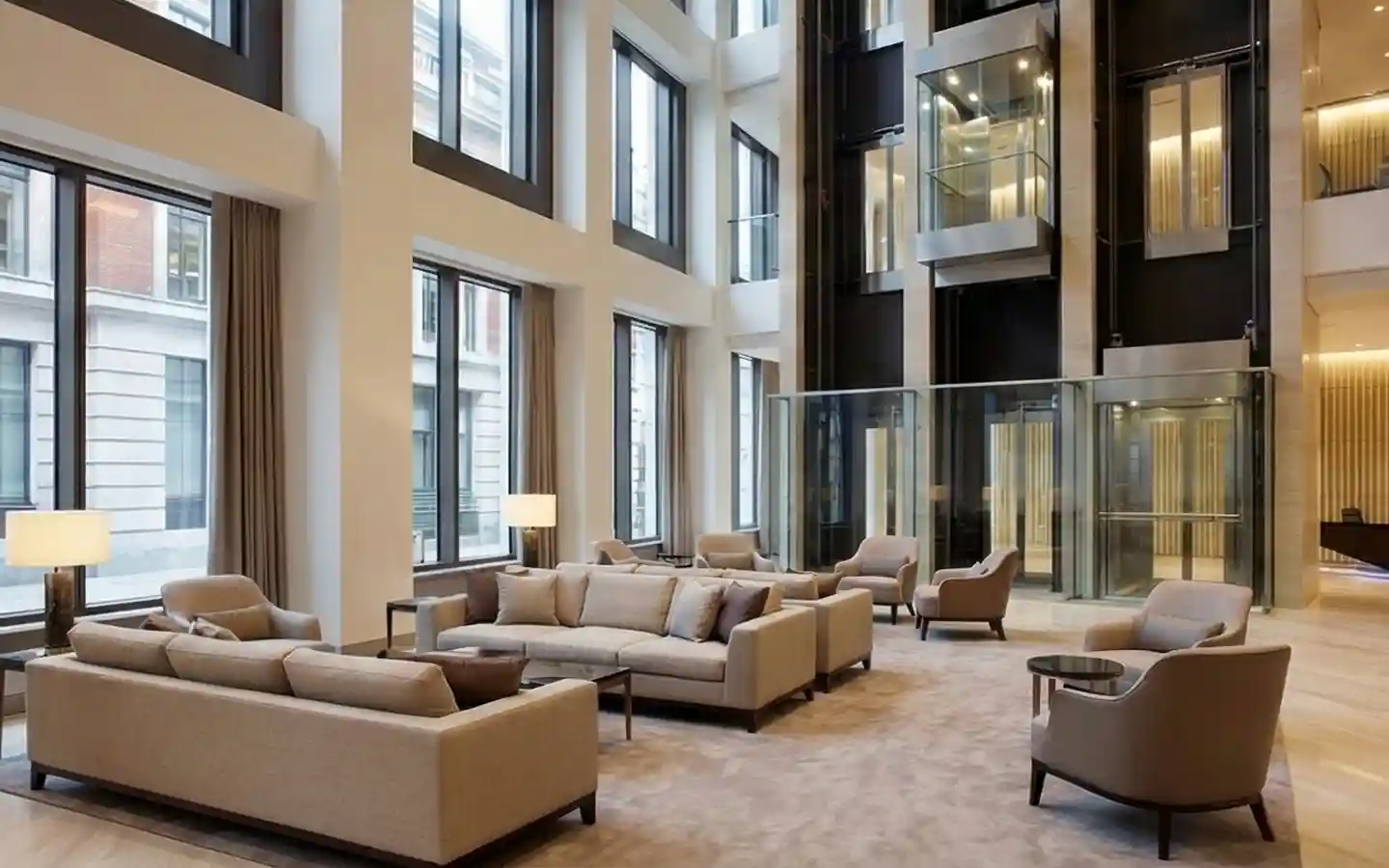 Luxurious modern hotel lobby featuring double-height ceilings, beige contemporary sofas, and glass observation elevators