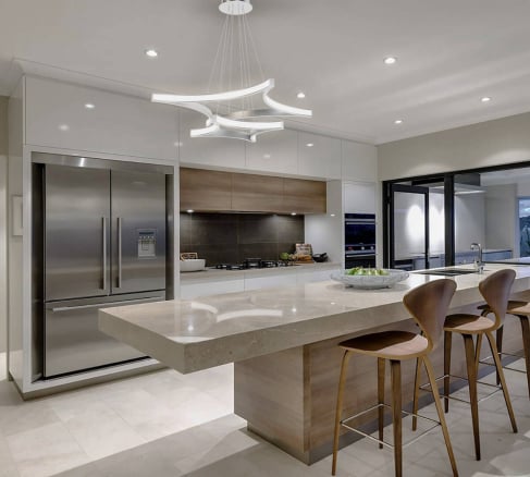 Modern luxury kitchen interior featuring a large marble-top island with wooden bar stools, high-gloss white cabinetry, integrated stainless steel appliances, and a unique contemporary wave pendant light
