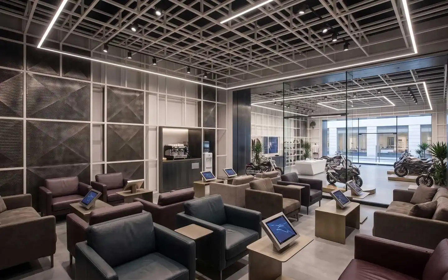 Modern luxury motorcycle showroom interior featuring industrial grid ceiling lights, leather lounge seating, and digital display kiosks