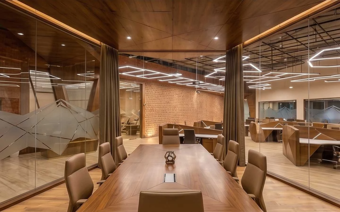 Modern luxury office interior featuring a large wooden conference table, geometric ceiling lighting, and glass partitions with brick accents