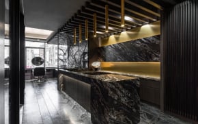 Modern luxury salon interior featuring a black marble reception desk, gold pendant lighting, and dark wood wall paneling