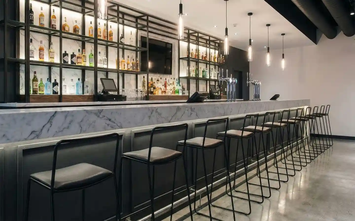 Modern pub interior featuring a white marble bar counter, black metal bar stools, and custom industrial shelving for liquor display