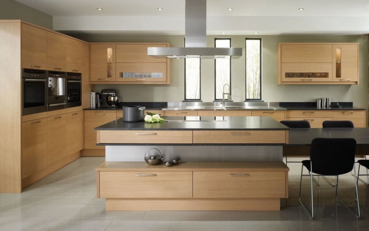 Spacious modern kitchen featuring natural oak wood cabinetry, a large central island with black stone countertops, and integrated stainless steel appliances
