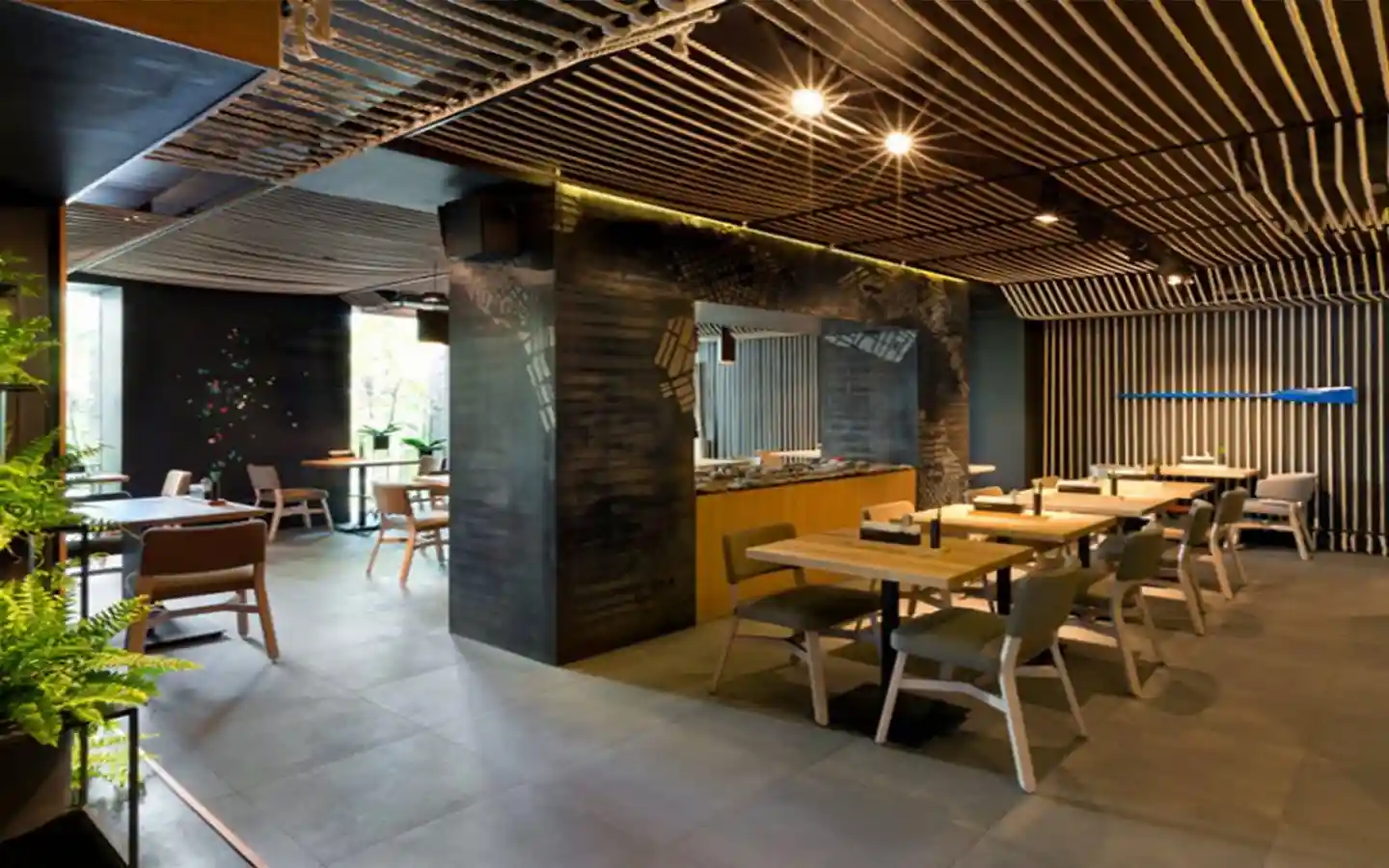 Contemporary restaurant interior featuring a decorative rope ceiling, vertical slat wall with a blue oar accent, indoor greenery, and minimalist wooden dining sets