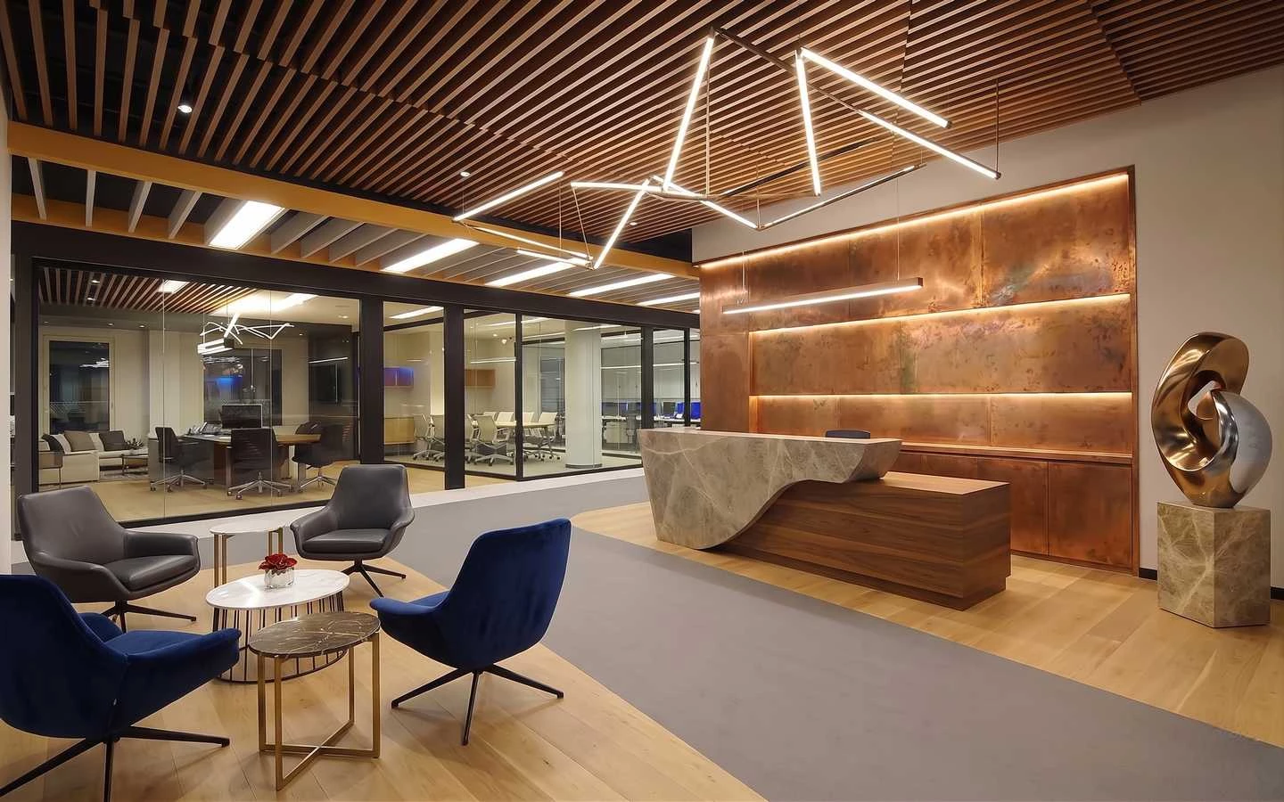 Modern luxury office reception area featuring a stone and wood reception desk, copper wall paneling, geometric LED lighting, and a contemporary waiting lounge with velvet chairs