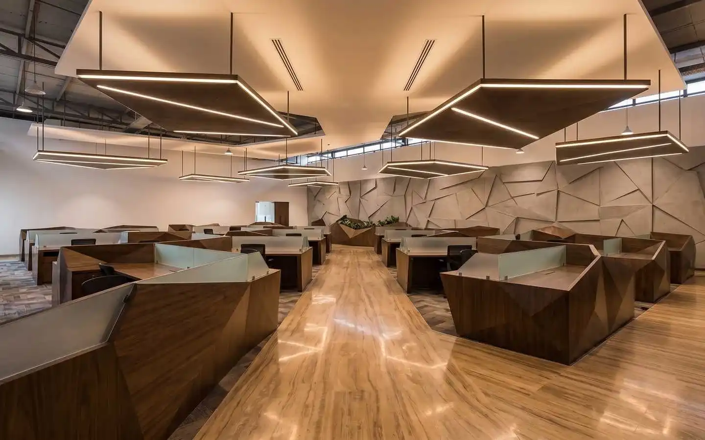 Modern open-plan commercial office interior featuring geometric wooden workstations, unique suspended linear lighting, and a textured 3D accent wall