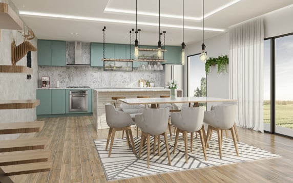 Bright, modern open-plan kitchen and dining area featuring muted teal cabinets, a large island, rustic exposed-bulb pendant lighting, and a white dining table with grey upholstered chairs on a geometric rug