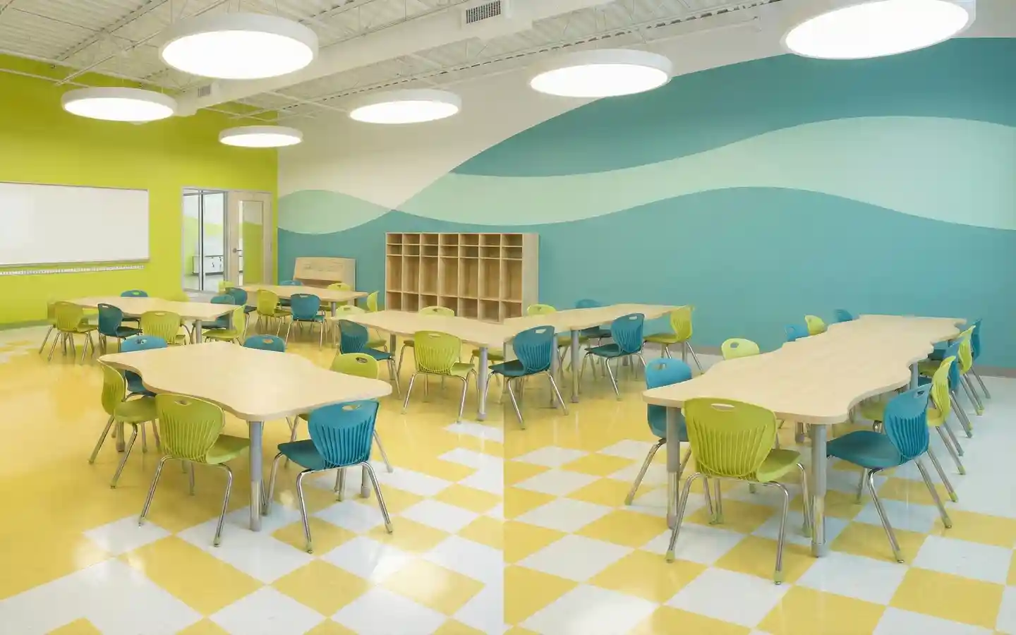 Modern elementary school classroom featuring ergonomic colorful chairs, wavy collaborative desks, and a bright yellow checkered floor