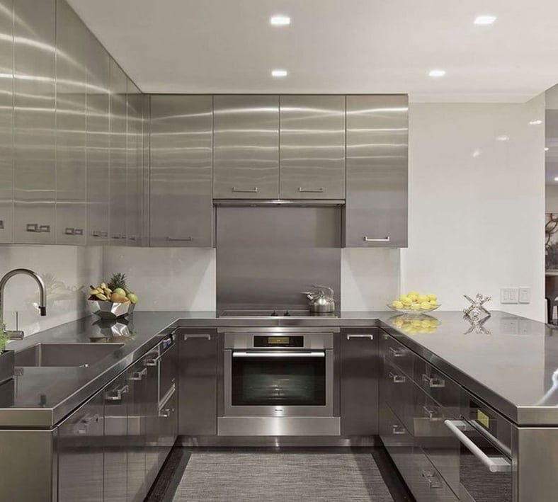 Modern U-shaped residential kitchen featuring full stainless steel cabinetry, integrated appliances, and sleek metallic countertops for a contemporary industrial look