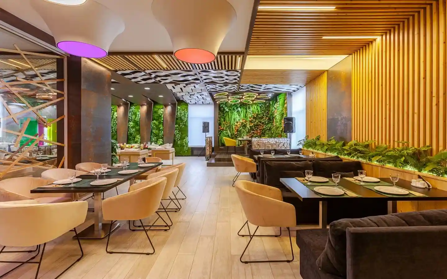 Modern restaurant dining area featuring a lush vertical green wall, wooden slat ceiling, and contemporary lounge seating