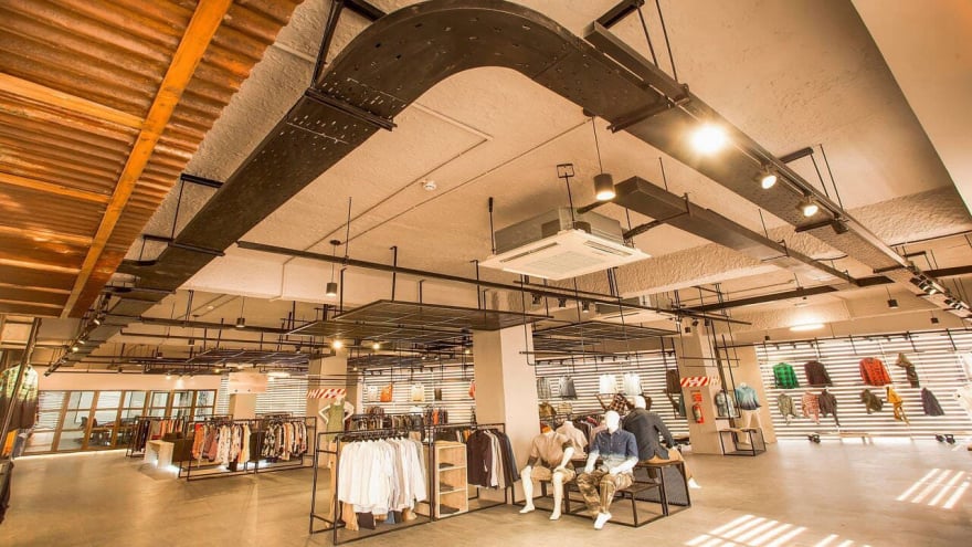 Spacious modern retail store interior with industrial ceiling design, clothing racks, mannequins, and wall displays of apparel in warm lighting
