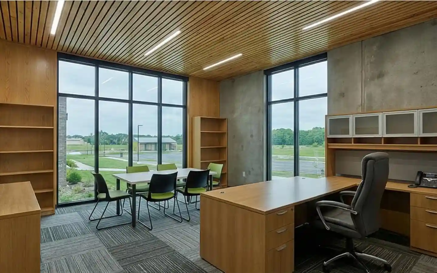 Modern school staff office featuring a wooden slat ceiling, large windows, oak desks, and a small meeting table