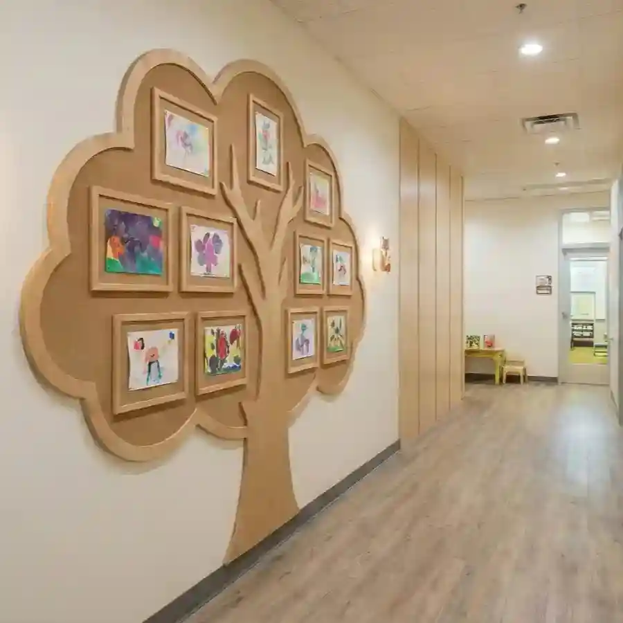 A tree-shaped corkboard wall display featuring framed student artwork in a modern school hallway with light wood flooring