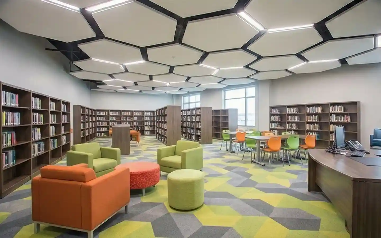 Modern school library interior featuring hexagonal ceiling lights, colorful lounge seating, and wooden bookshelves