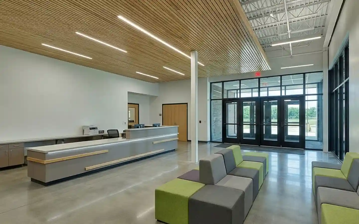 Modern school reception area featuring a wood slat ceiling, minimalist front desk, and colorful modular seating in a bright lobby
