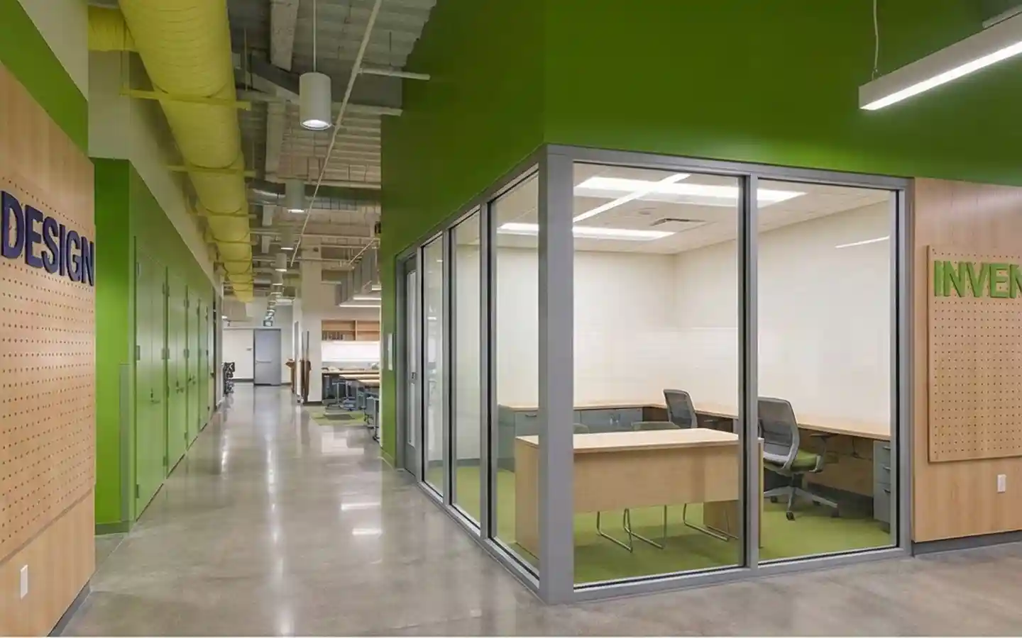 Modern school interior featuring a glass-walled STEM lab with wooden desks, green accent walls, and industrial exposed yellow ductwork in the hallway