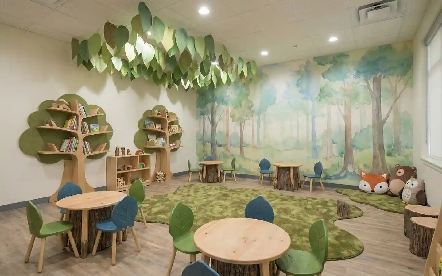 Modern preschool classroom with forest-themed interior design, featuring tree-shaped bookshelves, stump tables, and a woodland mural