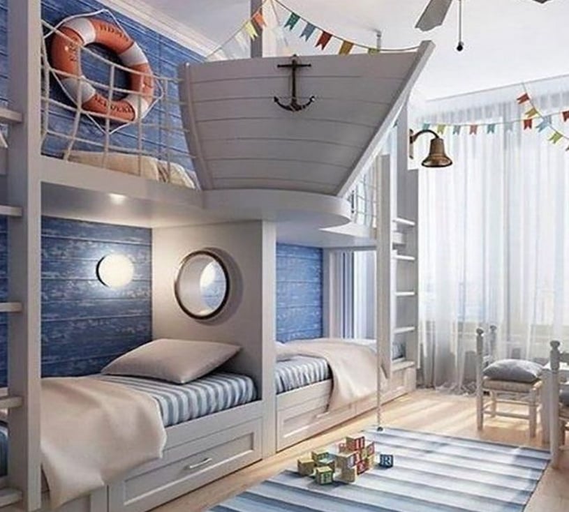 Custom nautical-themed kids bedroom featuring white ship-shaped bunk beds, blue wood-paneled walls, and coastal decor like a lifebuoy and anchor