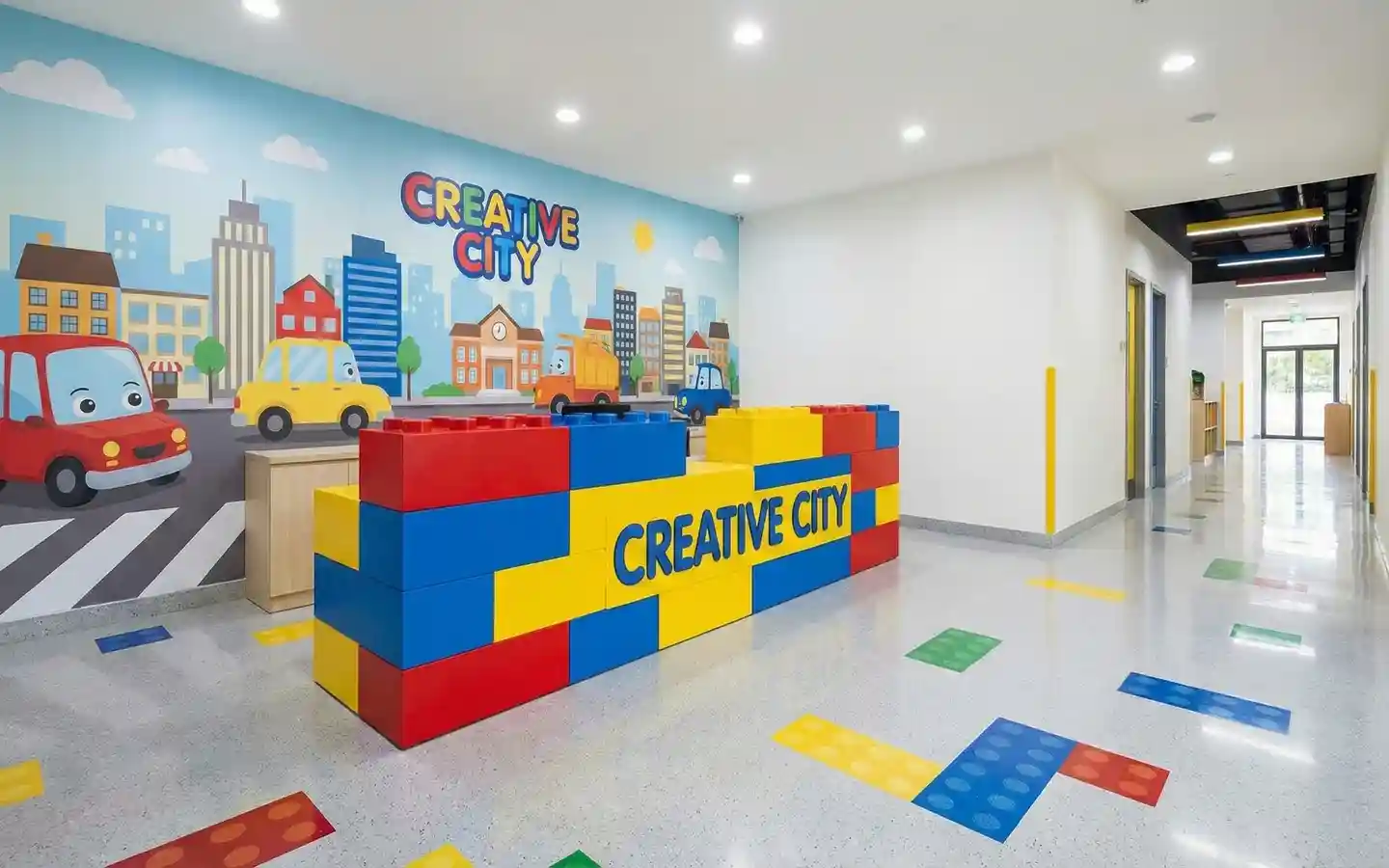 Colorful play school reception area featuring a building-block style desk, city-themed wall mural, and interactive floor graphics