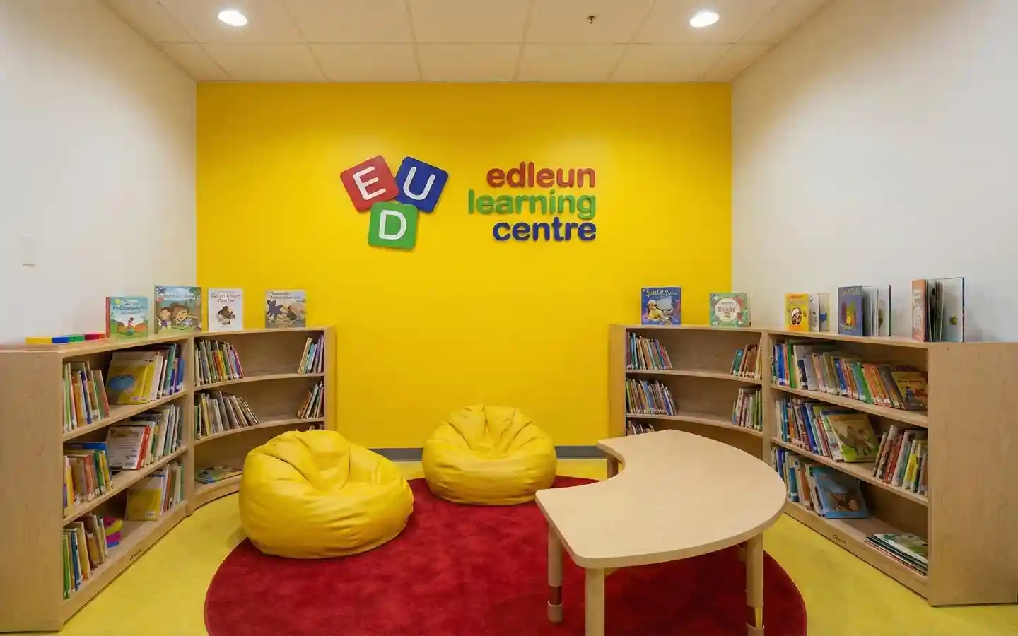 Vibrant kids' reading area in a learning center featuring yellow bean bags, curved wooden bookshelves, and a colorful accent wall