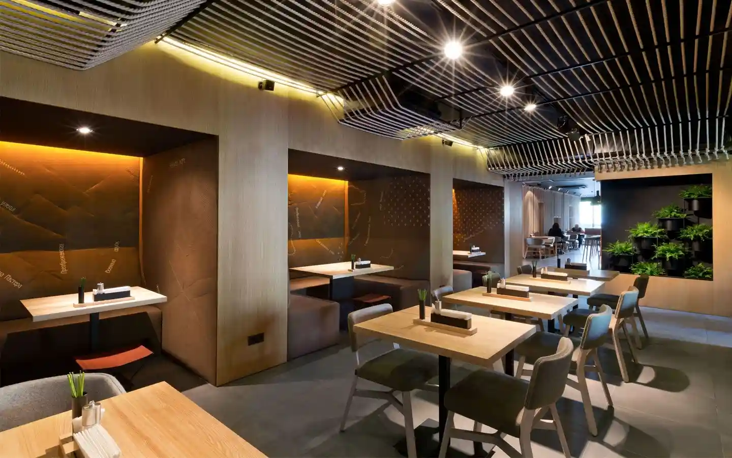 Restaurant interior featuring a warm wood slat ceiling, a vertical louvered feature wall with gold lighting, and a communal dining table with sake bottle display
