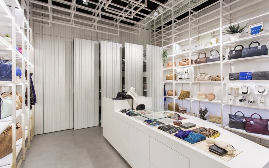 Retail store interior with glass display counter featuring accessories and handbags on organized white shelves