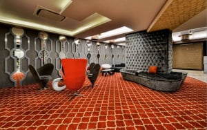 Retro-futuristic modern lounge interior with tufted sofa, geometric red carpet, hexagonal wall design, circular mirrors, and sculptural chairs