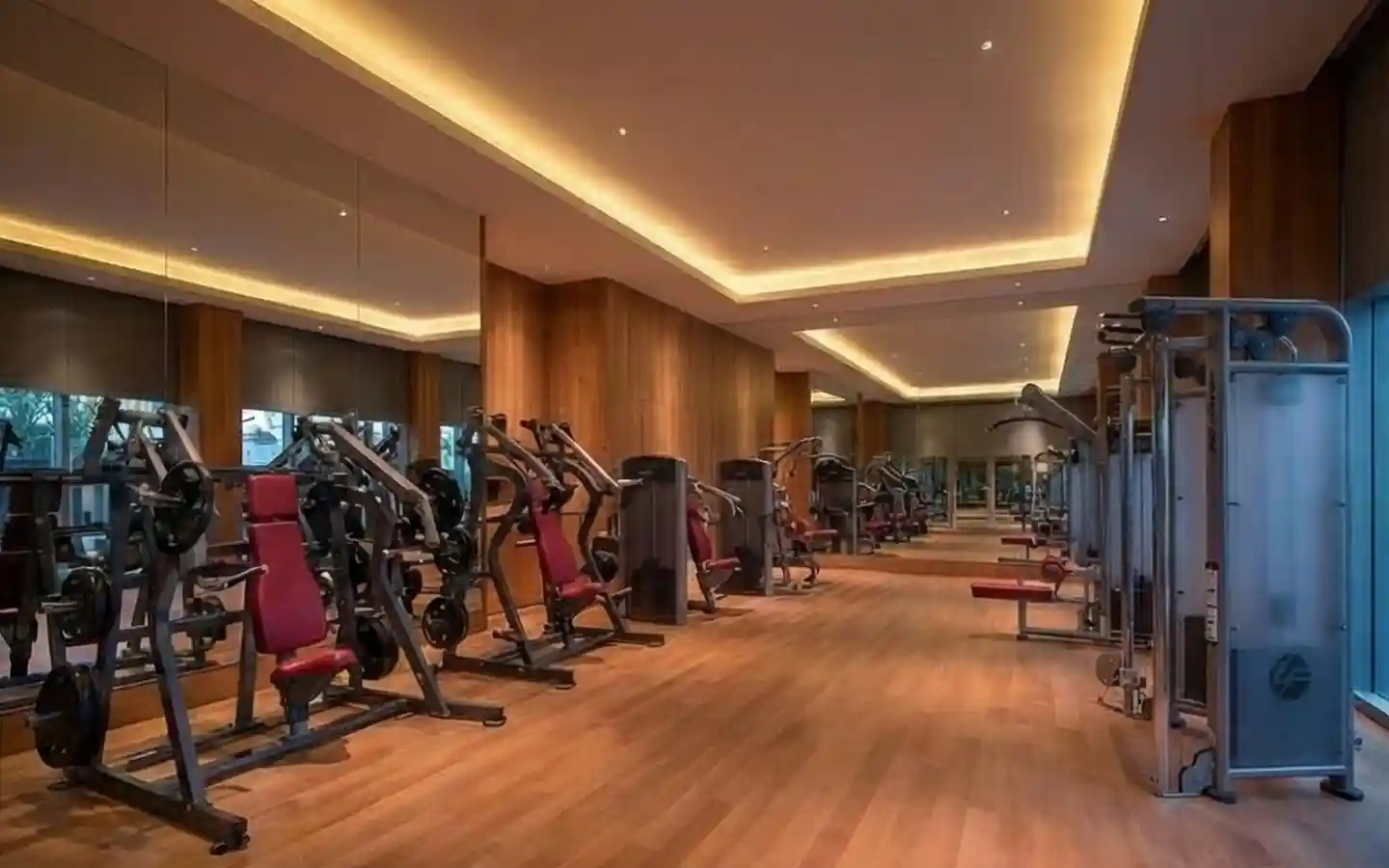 Sophisticated hotel gym interior featuring warm wood wall paneling, hardwood floors, and modern cove ceiling lighting with strength training equipment