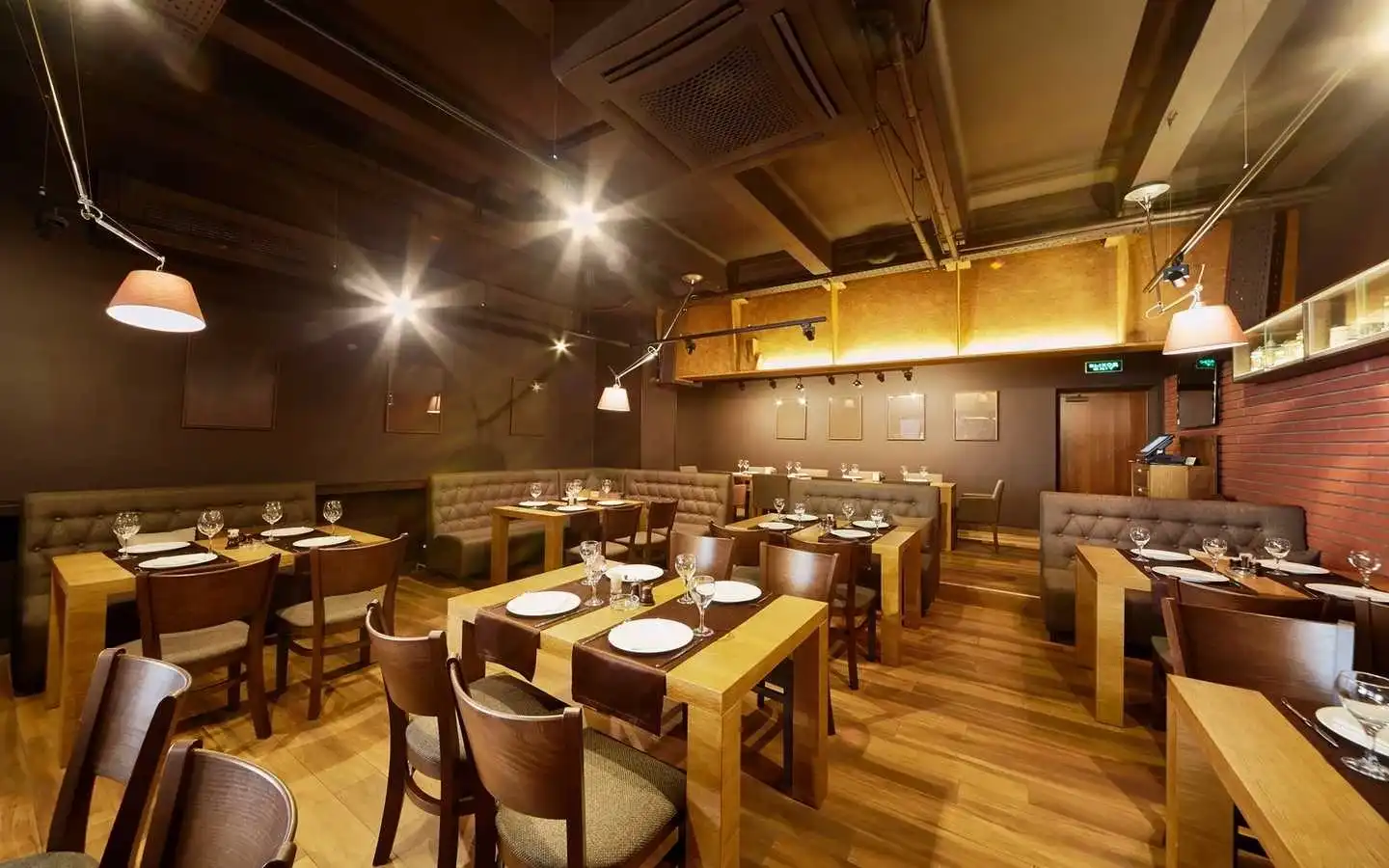 Upscale restaurant dining room interior featuring wooden tables, tufted leather booth seating, industrial ceiling accents, and warm pendant lighting