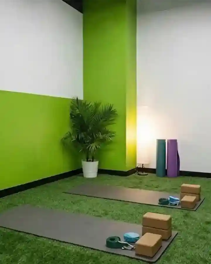 Minimalist yoga studio interior design featuring green artificial grass flooring, yoga mats, cork blocks, and a lime green accent wall