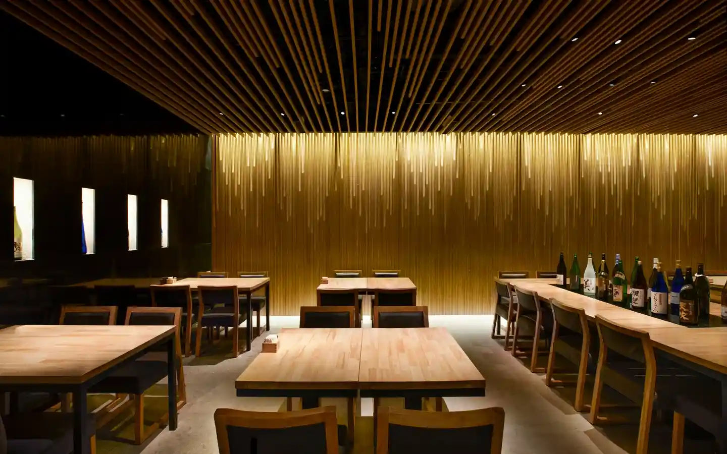 Minimalist restaurant interior featuring a dramatic timber batten ceiling, a gold-accented feature wall with waterfall lighting, and light wood dining tables